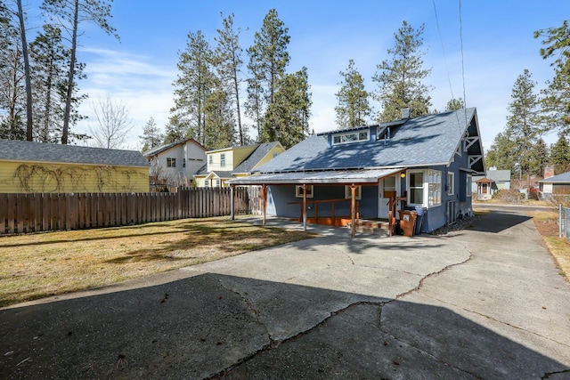 back of house with driveway, fence, roof with shingles, covered porch, and solar panels