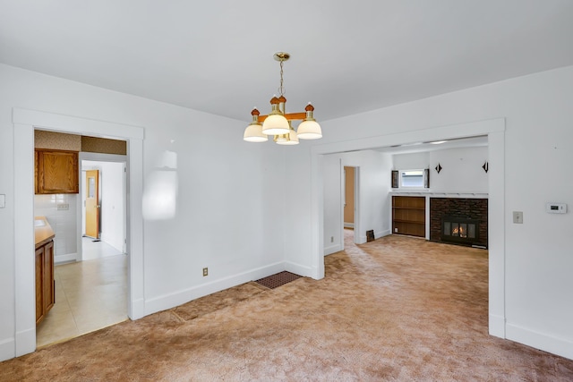 unfurnished dining area featuring a stone fireplace, an inviting chandelier, baseboards, and light carpet