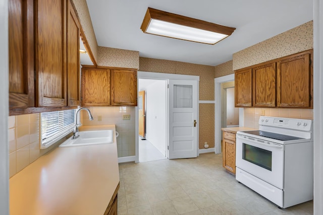 kitchen featuring brown cabinets, white electric stove, wallpapered walls, and a sink