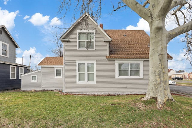 back of house featuring a lawn, a chimney, and roof with shingles