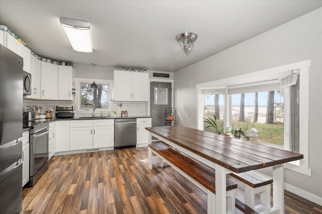 kitchen with dark countertops, a sink, backsplash, appliances with stainless steel finishes, and dark wood-style flooring