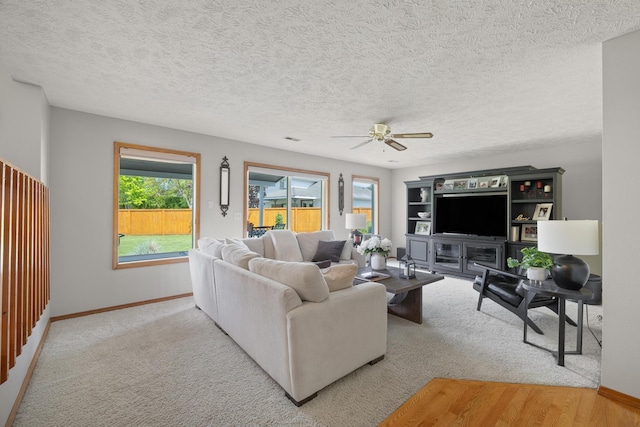 carpeted living area with a textured ceiling, baseboards, and ceiling fan