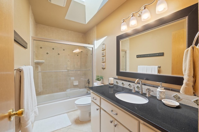 full bathroom with tile patterned flooring, toilet, a skylight, enclosed tub / shower combo, and vanity