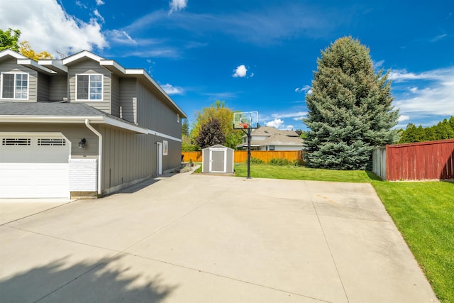 view of side of property featuring a lawn, driveway, fence, a storage shed, and a garage