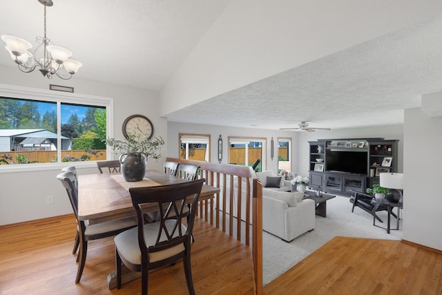 dining area featuring vaulted ceiling, ceiling fan with notable chandelier, light wood finished floors, and a textured ceiling