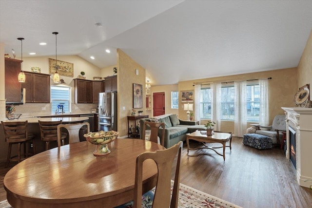 dining space with lofted ceiling, recessed lighting, wood finished floors, and a lit fireplace