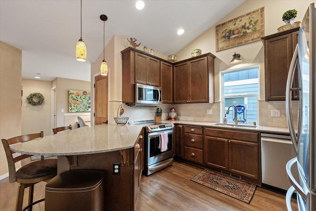 kitchen featuring lofted ceiling, a kitchen breakfast bar, a peninsula, stainless steel appliances, and a sink