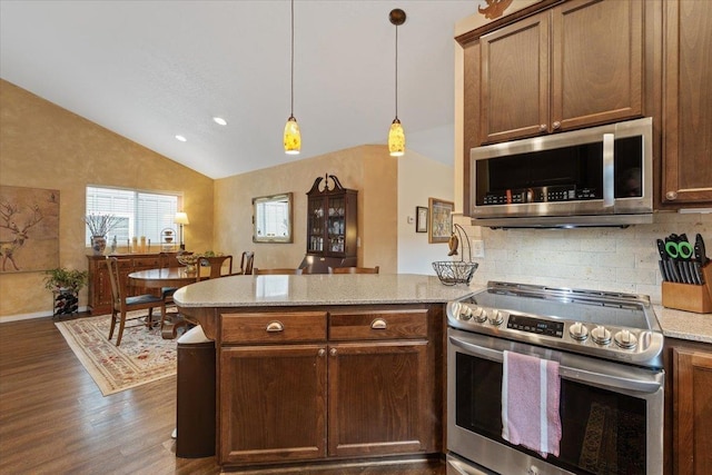 kitchen with a peninsula, stainless steel appliances, vaulted ceiling, dark wood-type flooring, and tasteful backsplash