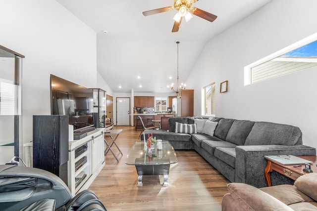 living area with light wood finished floors, high vaulted ceiling, and ceiling fan with notable chandelier