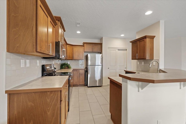 kitchen featuring a breakfast bar area, brown cabinetry, a peninsula, a sink, and appliances with stainless steel finishes