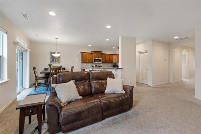 living room with arched walkways, visible vents, recessed lighting, and light carpet