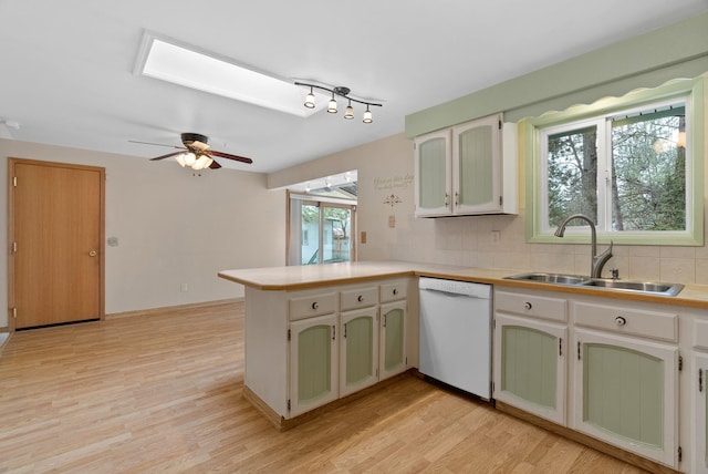 kitchen with decorative backsplash, light wood-style flooring, a peninsula, white dishwasher, and a sink