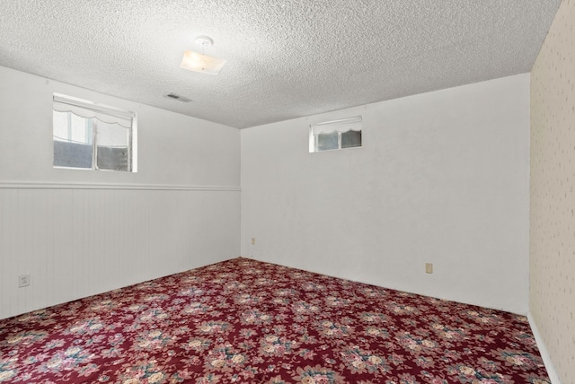 basement featuring visible vents, a textured ceiling, and carpet floors