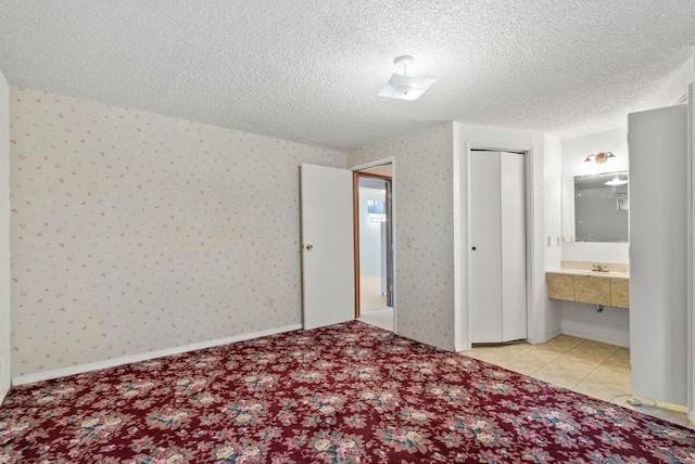 unfurnished bedroom featuring wallpapered walls, connected bathroom, baseboards, and a textured ceiling