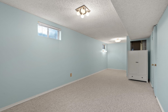 basement featuring baseboards, light colored carpet, and a textured ceiling