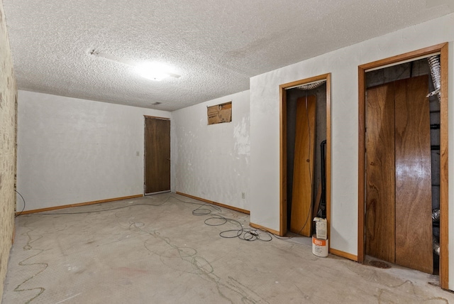 empty room with a textured ceiling, unfinished concrete flooring, and baseboards