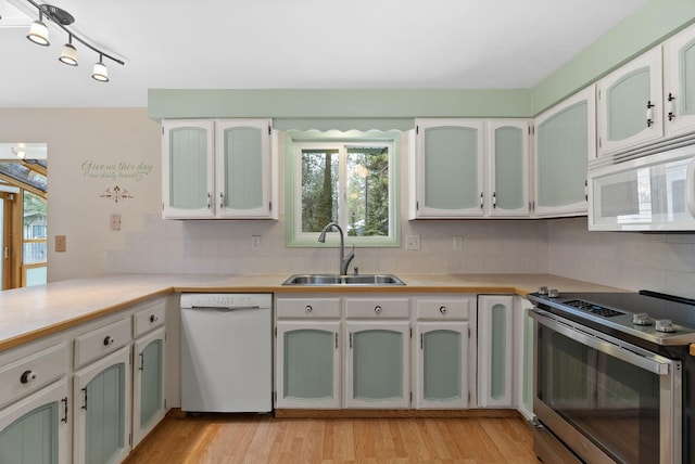 kitchen with a sink, light wood-style floors, white appliances, and backsplash