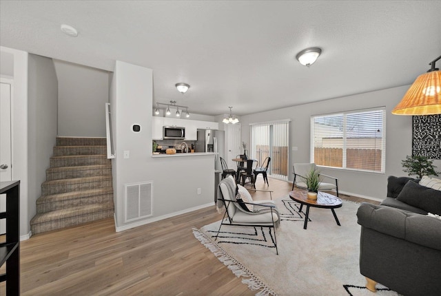 living area with stairway, baseboards, visible vents, light wood finished floors, and a chandelier