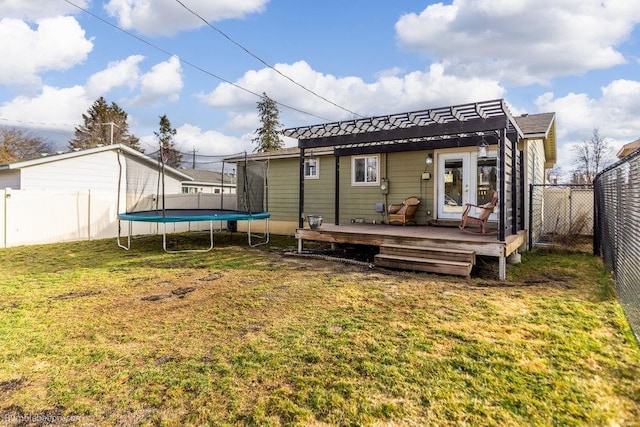 rear view of property with a trampoline, a lawn, a fenced backyard, and a wooden deck