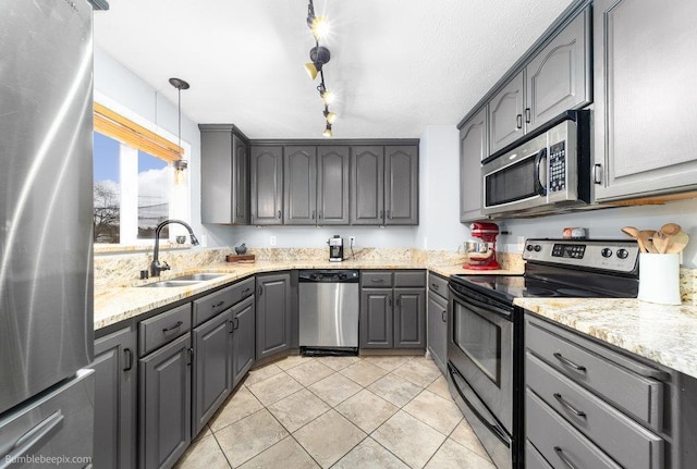 kitchen featuring gray cabinets, light stone countertops, stainless steel appliances, and a sink