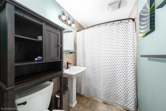 full bathroom featuring a shower with shower curtain, visible vents, a sink, tile walls, and toilet