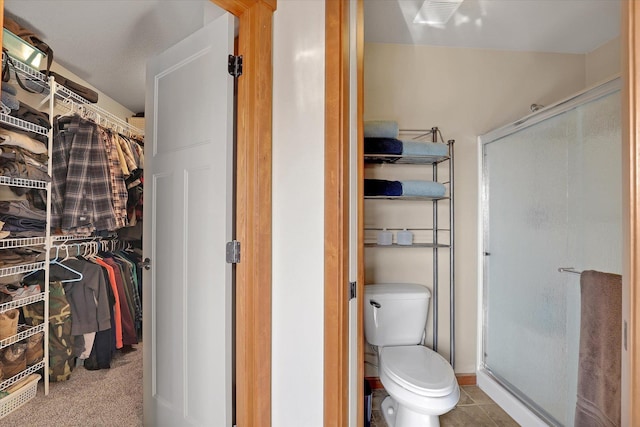 bathroom featuring a walk in closet, a shower stall, toilet, and tile patterned floors