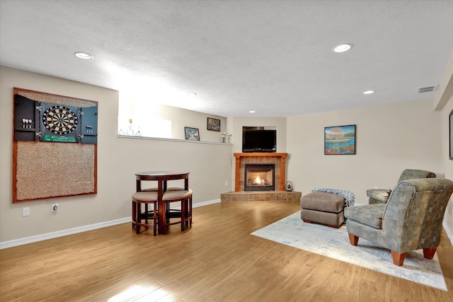 sitting room with visible vents, a tiled fireplace, a textured ceiling, wood finished floors, and baseboards