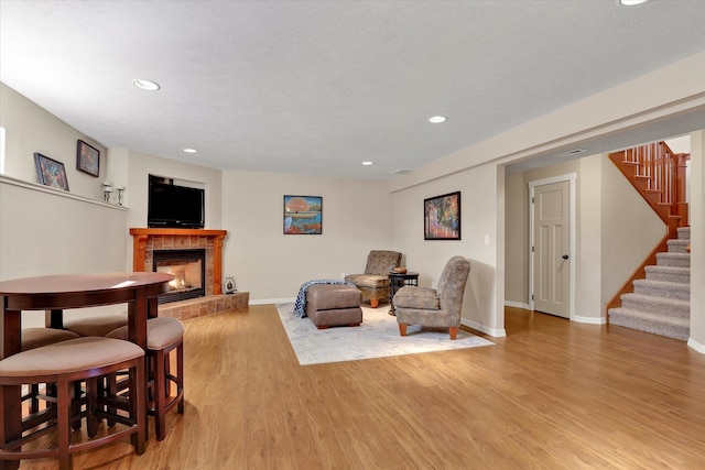 living room featuring stairway, baseboards, recessed lighting, light wood-style floors, and a tiled fireplace