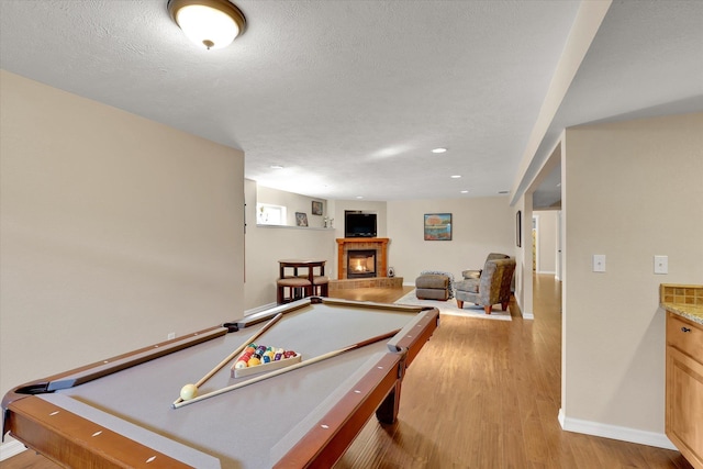 game room featuring a textured ceiling, a fireplace, pool table, and light wood finished floors