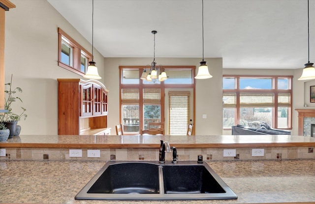 kitchen with a tile fireplace, hanging light fixtures, light countertops, a sink, and a notable chandelier