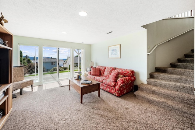 living area featuring visible vents, carpet floors, a textured ceiling, and stairway