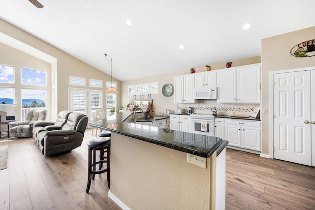 kitchen with vaulted ceiling, light wood-style flooring, a kitchen breakfast bar, white cabinets, and white appliances