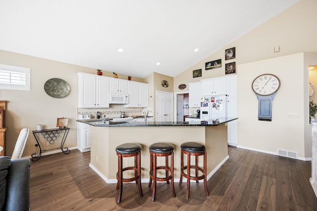 kitchen with visible vents, dark wood finished floors, a breakfast bar area, white appliances, and white cabinetry