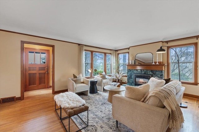 living area with baseboards, visible vents, a premium fireplace, light wood-style flooring, and crown molding