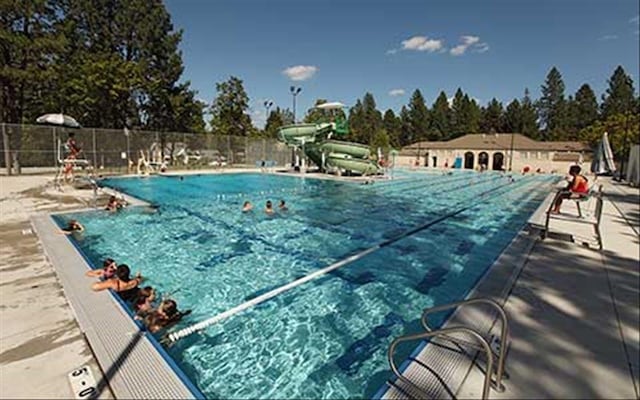 pool with a patio, a water slide, and fence