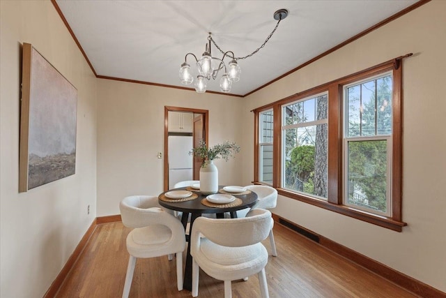 dining room with visible vents, baseboards, ornamental molding, an inviting chandelier, and wood finished floors