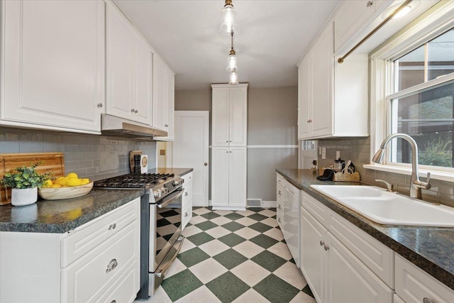 kitchen with dark countertops, under cabinet range hood, light floors, gas stove, and a sink