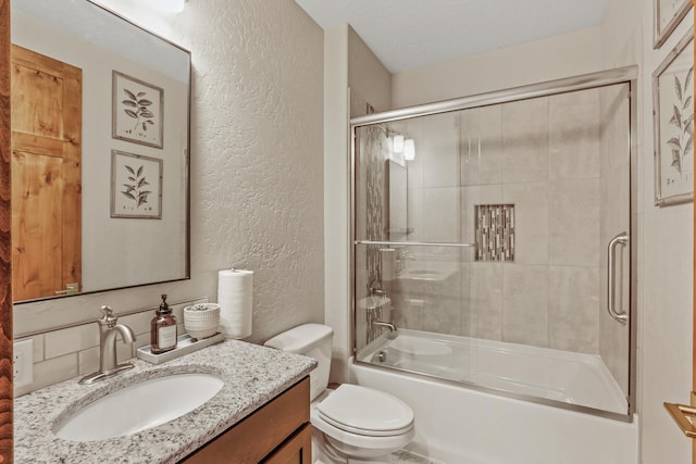 full bathroom with combined bath / shower with glass door, toilet, vanity, and a textured wall