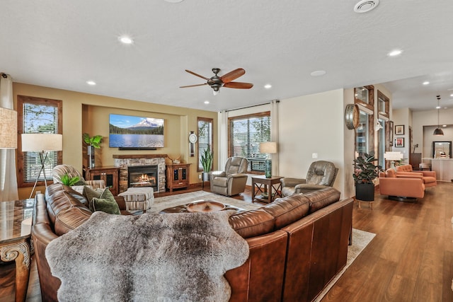 living room featuring a stone fireplace, recessed lighting, ceiling fan, and wood finished floors