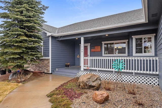 entrance to property featuring stone siding, a porch, and a shingled roof