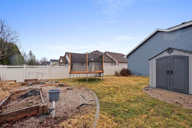 view of yard featuring a trampoline, a fenced backyard, a storage shed, a vegetable garden, and an outdoor structure