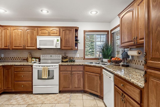 kitchen with a sink, decorative backsplash, white appliances, and brown cabinetry