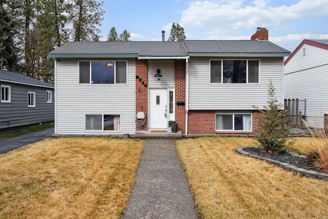 split foyer home featuring brick siding, a chimney, and a front lawn