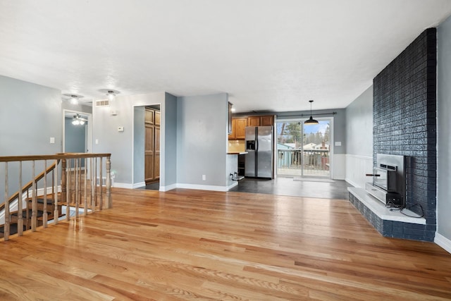 unfurnished living room with visible vents, a large fireplace, light wood-style floors, and baseboards