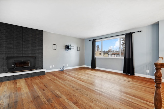 unfurnished living room featuring baseboards, a brick fireplace, and wood finished floors