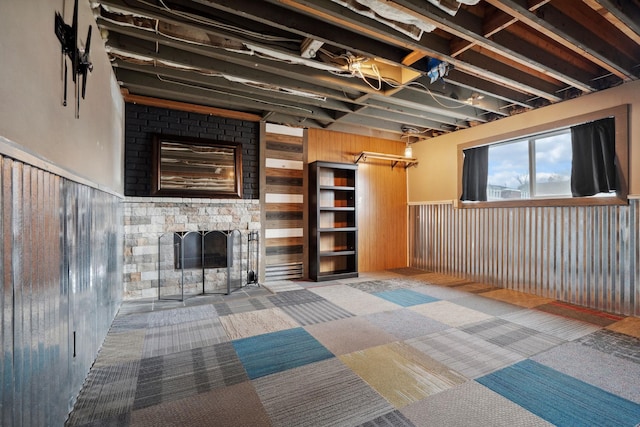 basement featuring a stone fireplace, wood walls, and carpet floors