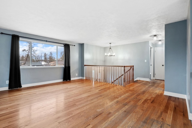 empty room featuring a chandelier, baseboards, a textured ceiling, and wood finished floors