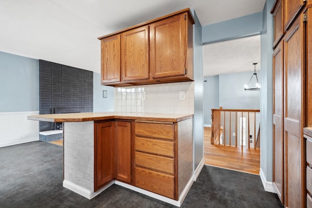 kitchen featuring brown cabinetry, a wainscoted wall, light countertops, and decorative backsplash