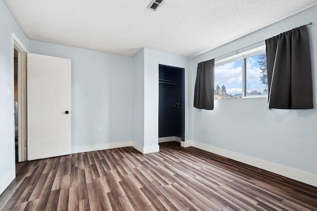 unfurnished bedroom with wood finished floors, visible vents, baseboards, a closet, and a textured ceiling