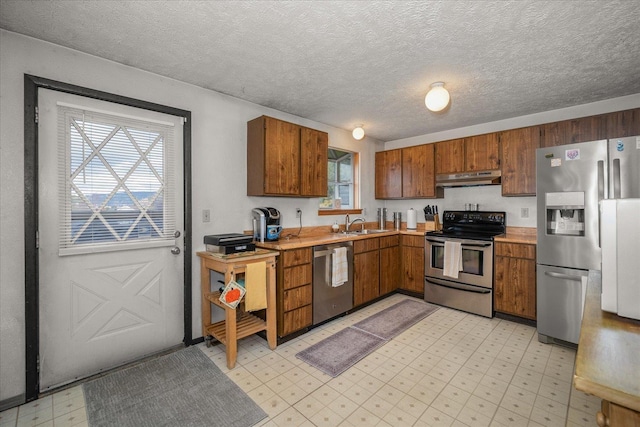 kitchen featuring under cabinet range hood, light floors, light countertops, stainless steel appliances, and a sink